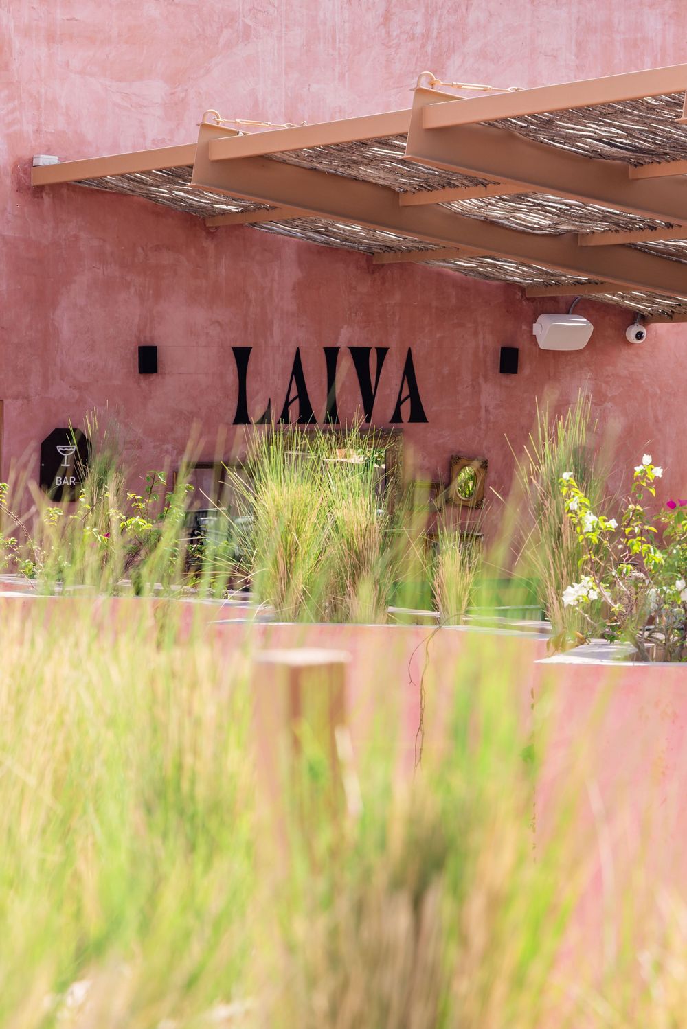 Pink stucco wall with LAIVA sign, wooden pergola, and ornamental grasses in foreground.