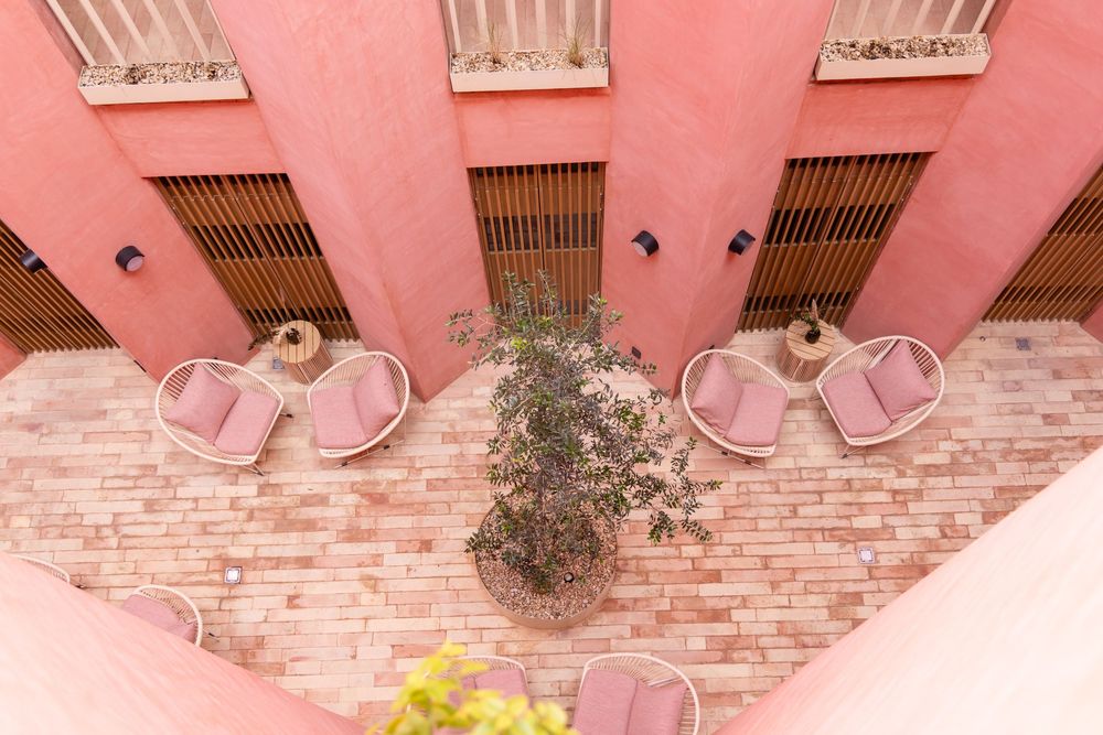 Aerial view of a pink courtyard with round cushioned chairs and a central potted plant.