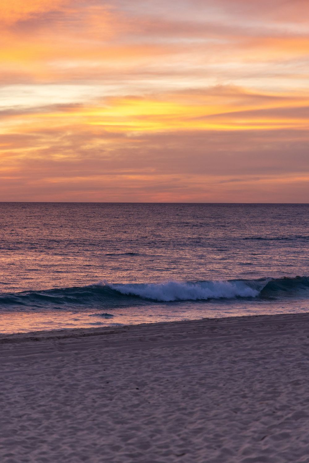 Vibrant sunset over calm ocean waves with golden orange sky reflecting on sandy beach shoreline.