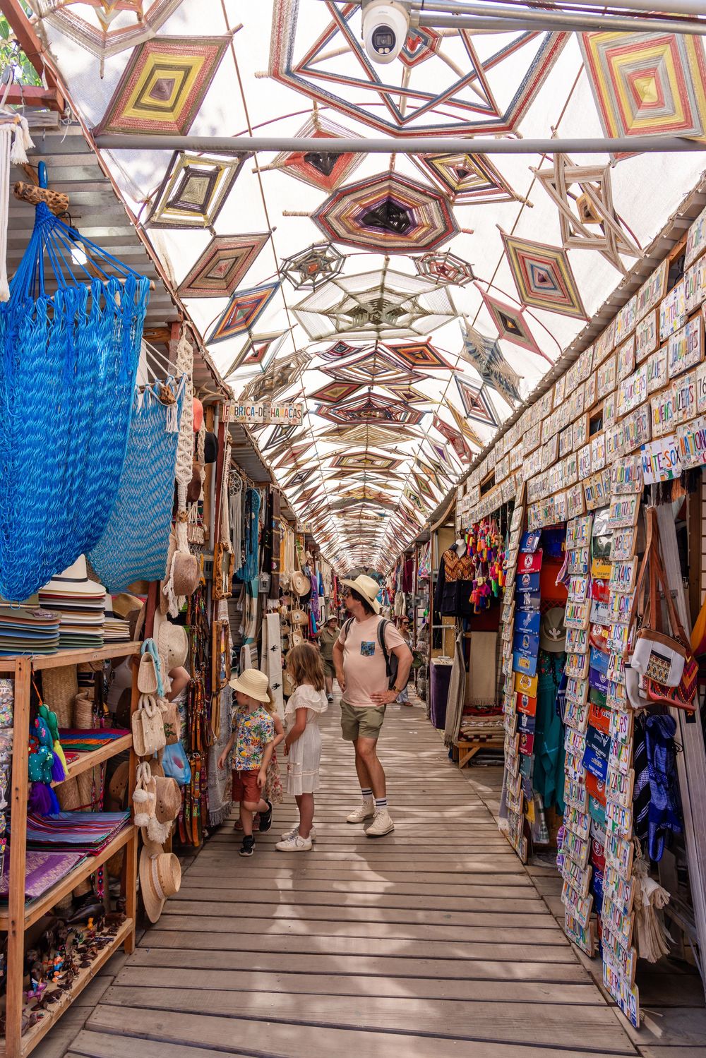 Colorful covered outdoor market corridor with handicrafts, bags, and decorative geometric ceiling.