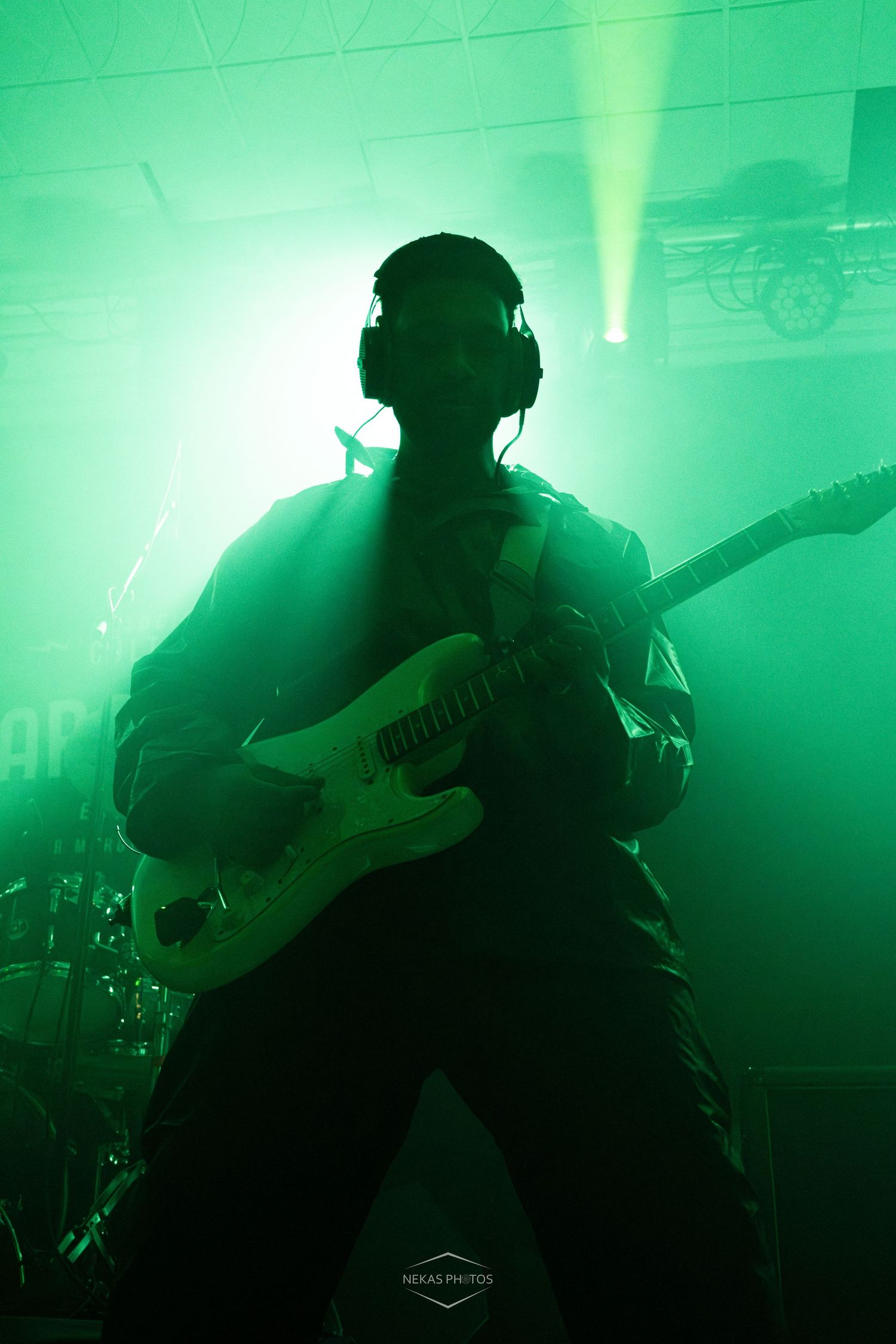 Silhouetted guitarist performing on stage under dramatic green lighting with headphones on.