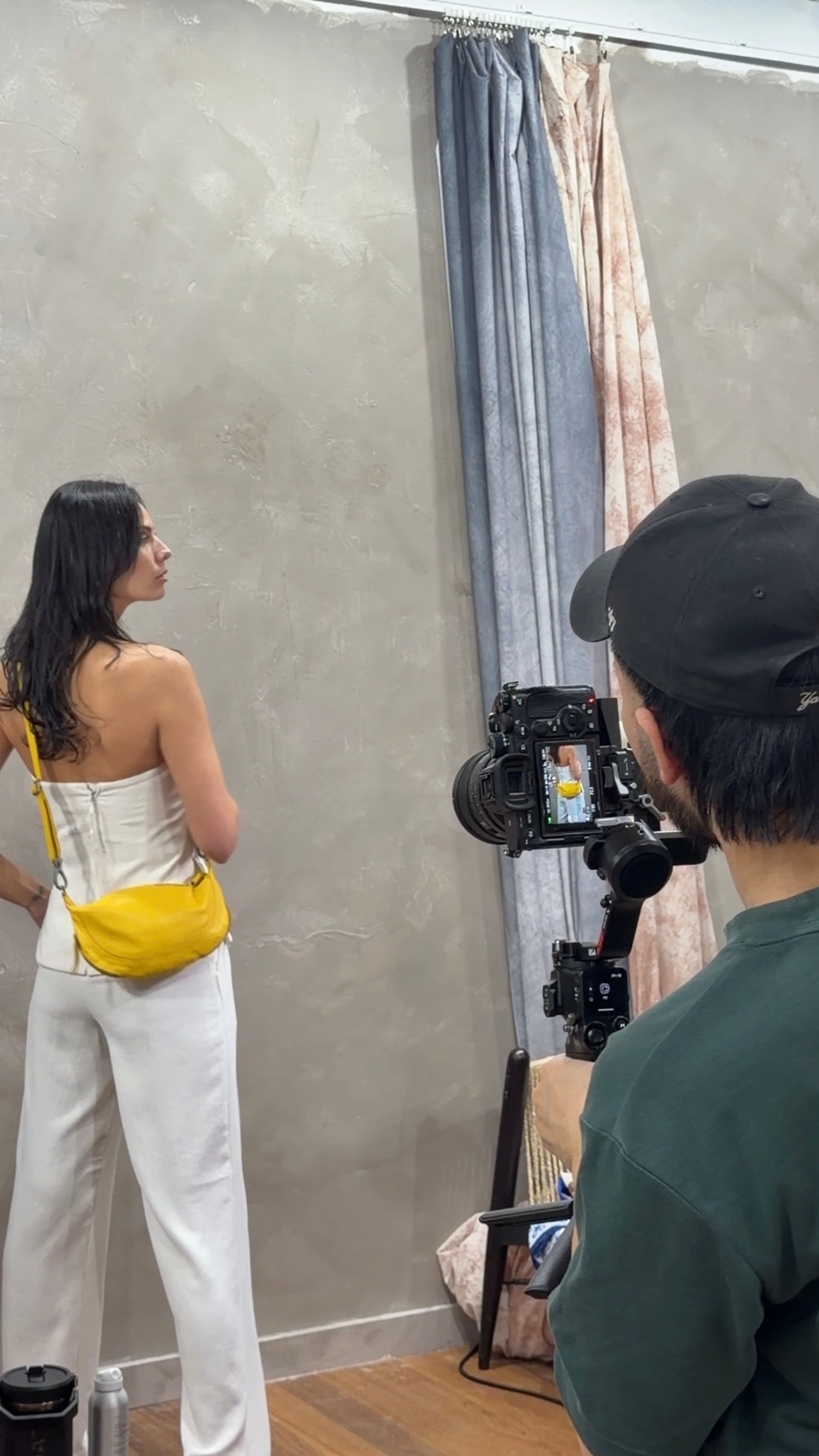 Behind the scenes photo shoot with model in yellow bag and white outfit being filmed.