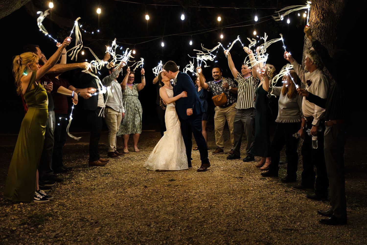 A celebratory wedding sparkler exit at an Austin, Texas venue, capturing the bride and groom kissing as guests cheer with streamers and spar