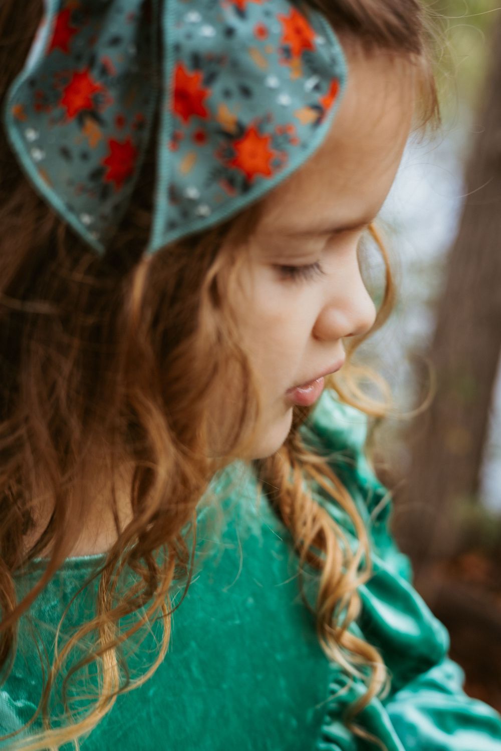 A documentary-style close-up portrait of a young girl with a floral bow in her hair during an outdoor lifestyle session in Central Texas.