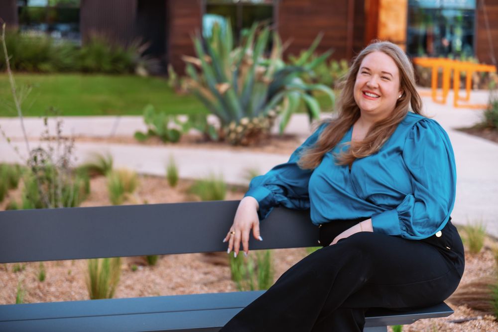 A professional lifestyle portrait of a woman sitting on an outdoor bench in a modern Austin, Texas courtyard.