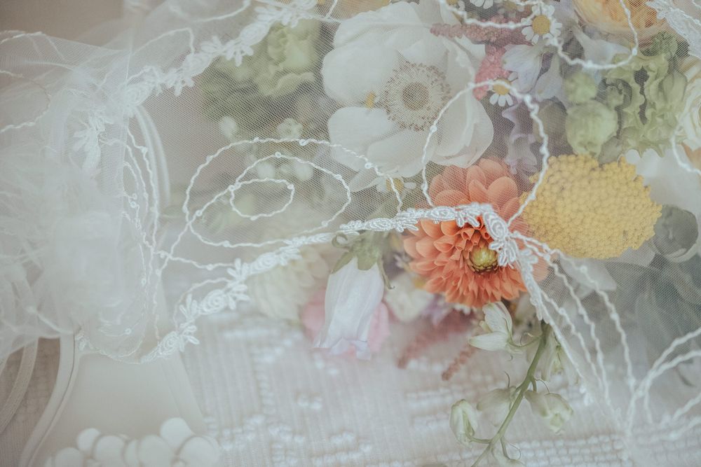 Elegant wedding bouquet with peach dahlia and white flowers draped under delicate lace veil.