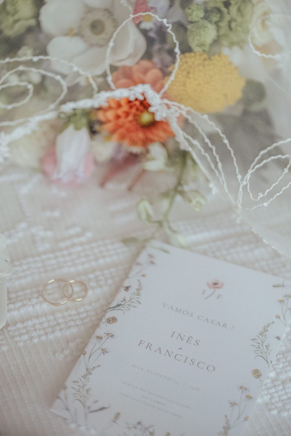 Elegant wedding flat lay with floral bouquet, gold rings, and Ines & Francisco ceremony program on white lace fabric.