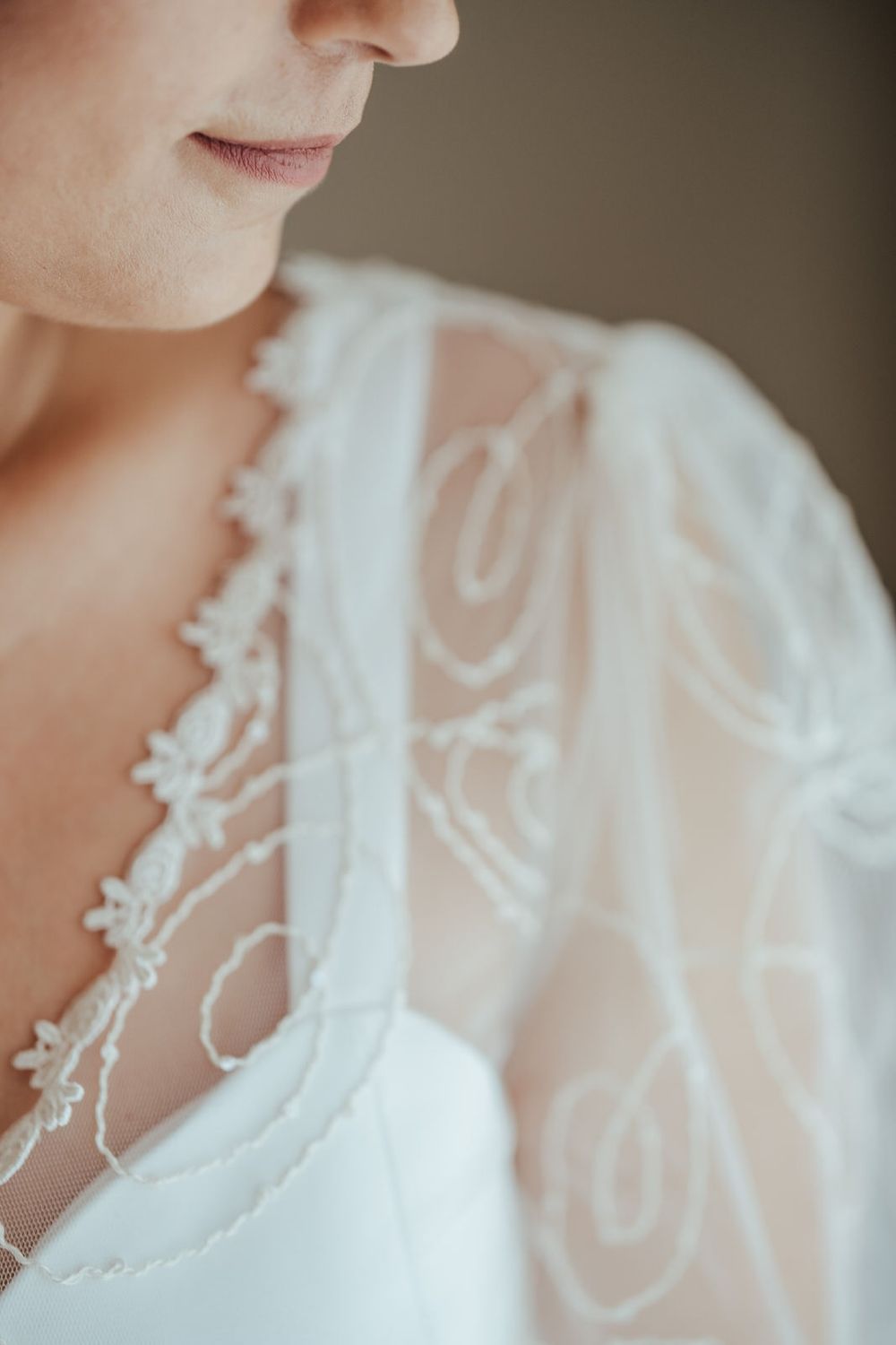 Close-up of a bride in a white lace wedding dress with delicate floral embroidery and beaded details.