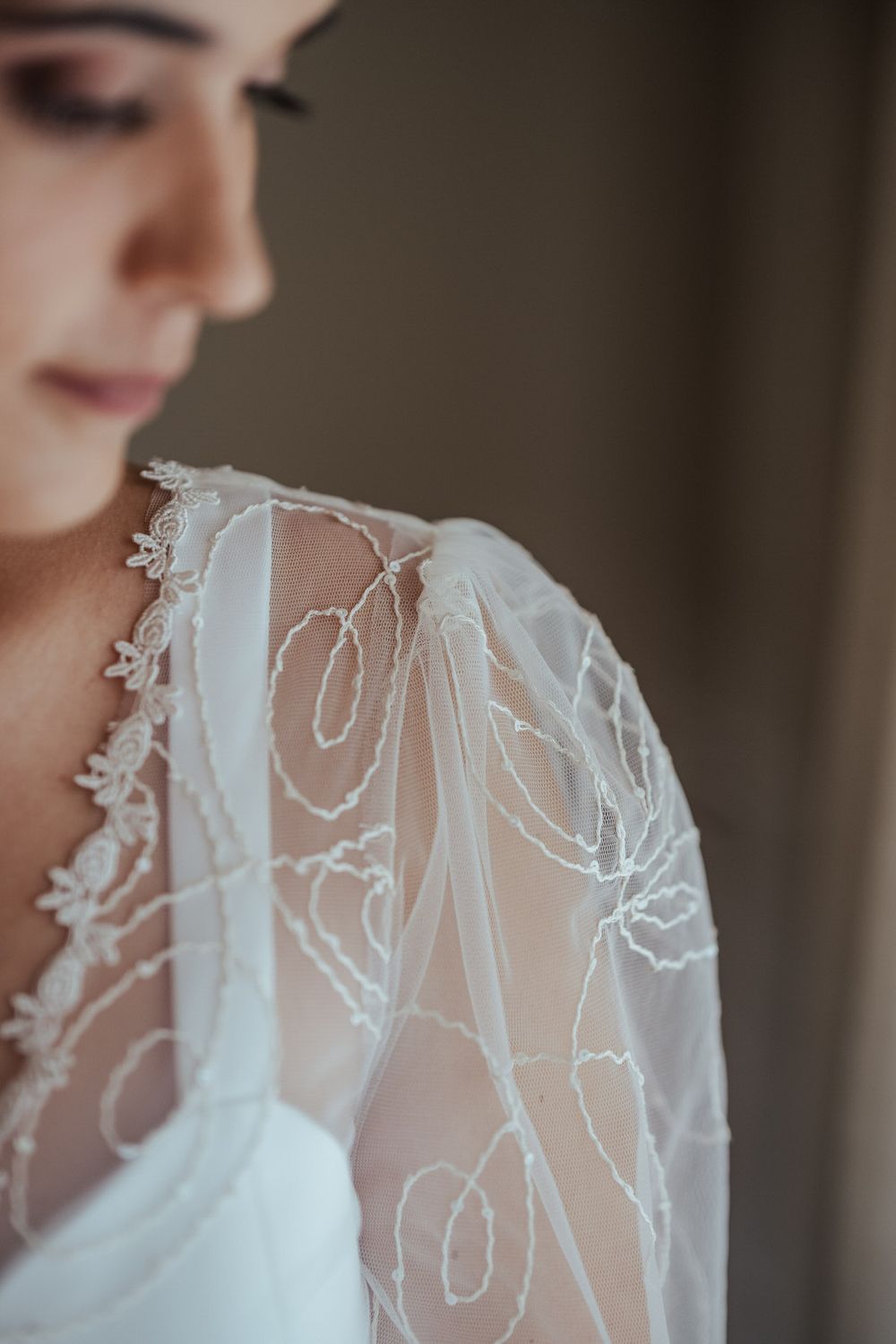 Close-up of a bride wearing an elegant white lace wedding dress with sheer embroidered sleeves.