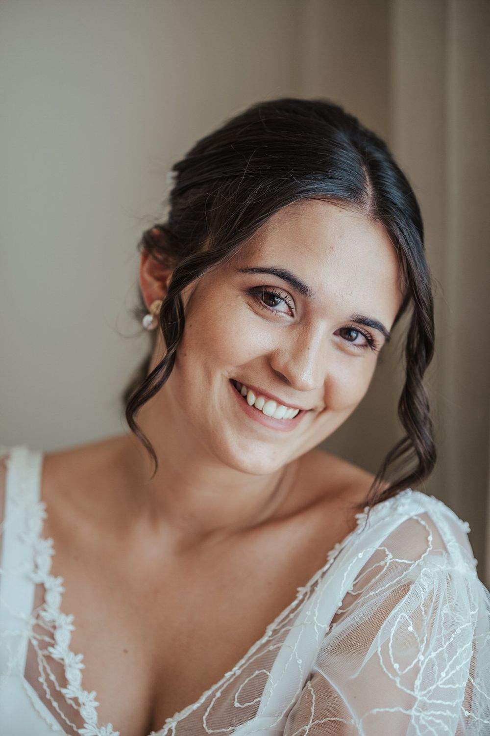 Beautiful smiling bride with dark hair wearing a white lace wedding gown with sheer sleeves.