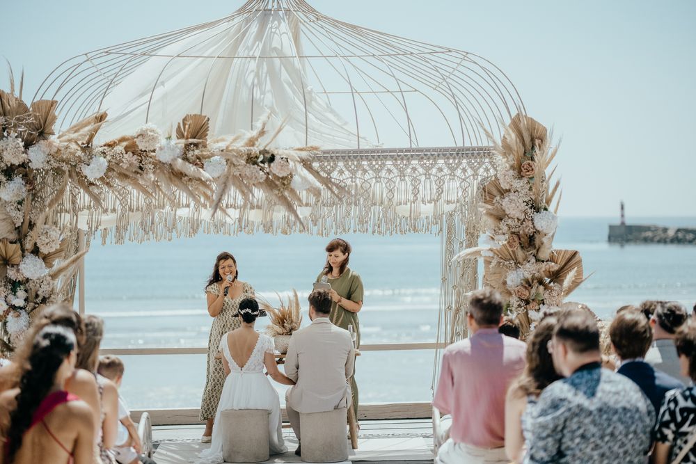 Romantic beachside wedding ceremony under a macrame boho arch with pampas grass and ocean backdrop.