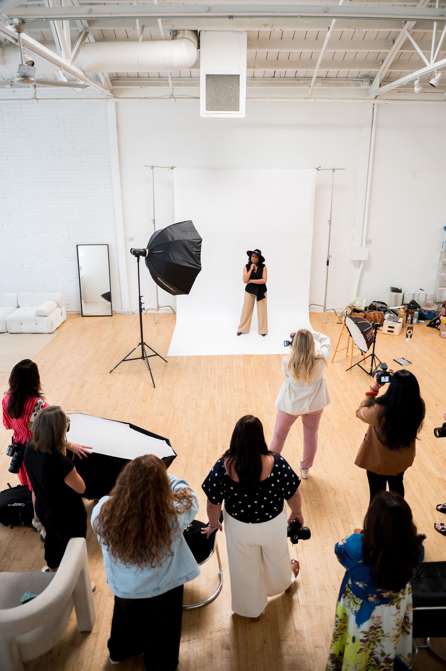 Professional photo shoot in a bright studio with a model on white backdrop, surrounded by photographers and lighting equipment.