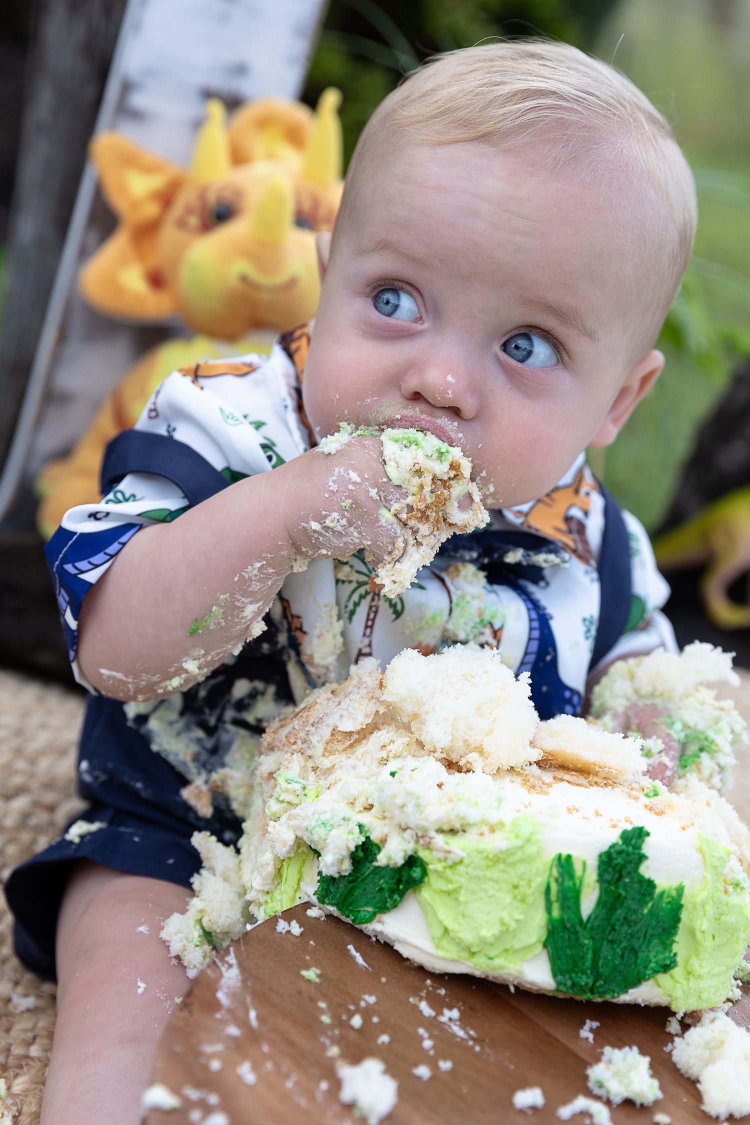 Little boy smashing a cake at a dinosaur cake smash and pushing cake into his mouth.