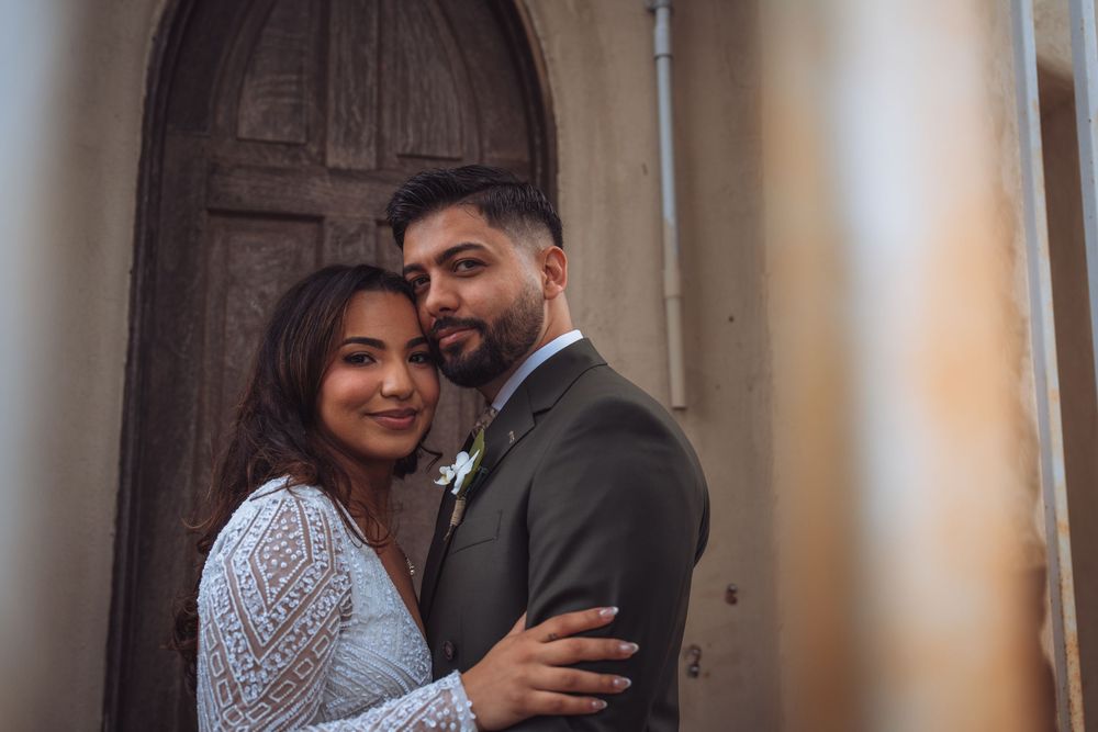 Couple in wedding attire embracing tenderly in front of vintage wooden door.