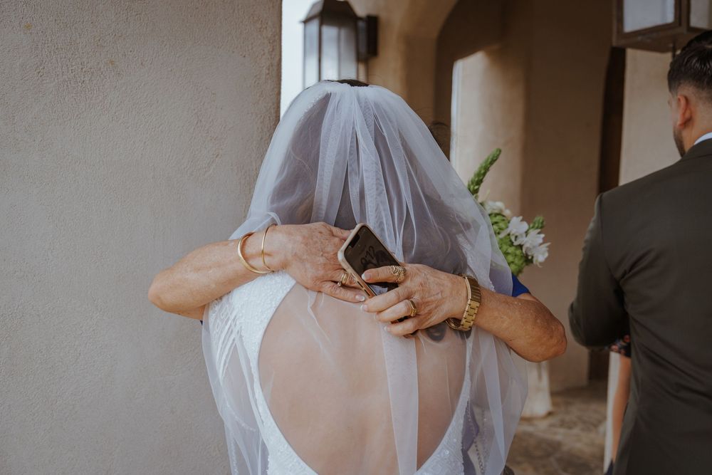 Bride in white backless wedding dress with veil, hands adjusting gown from behind on wedding day.