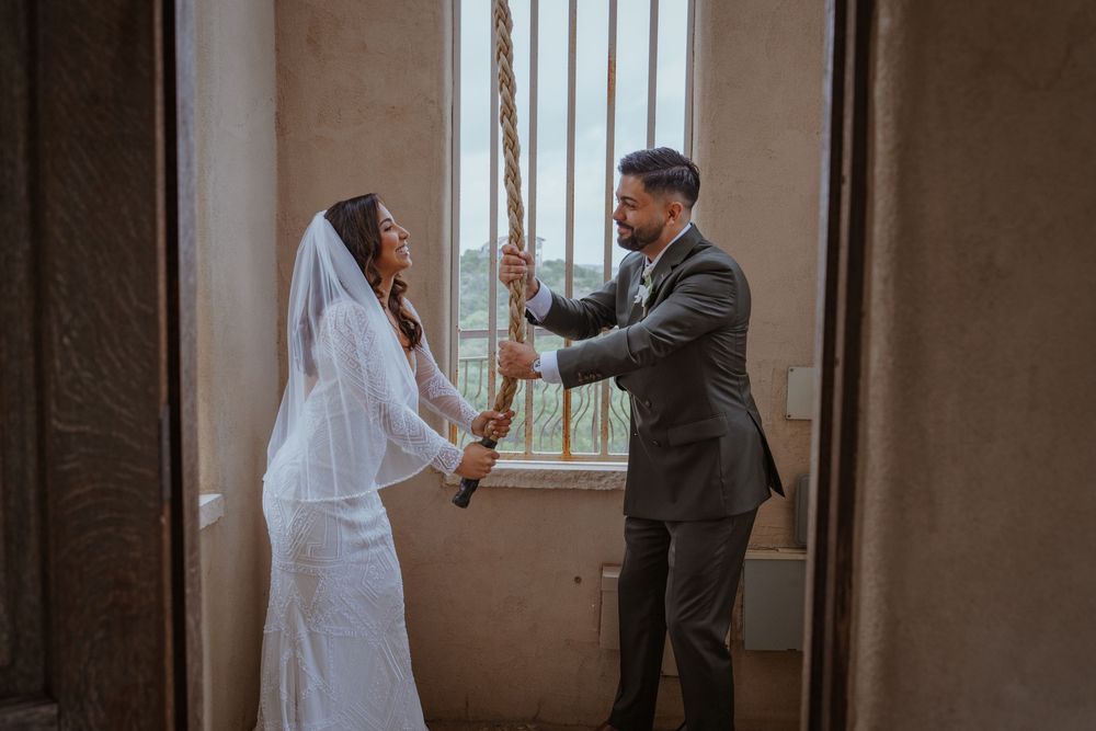 Bride and groom share a romantic moment pulling a rope together near a window in a rustic wedding venue.