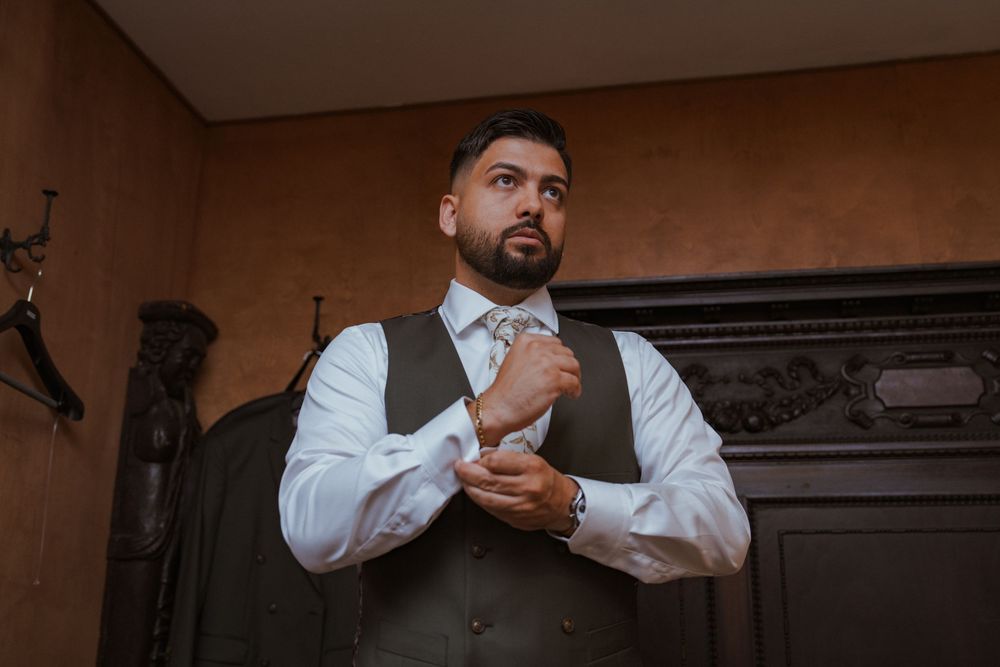 Groom in a gray vest and white dress shirt adjusting his cufflinks before the wedding ceremony.
