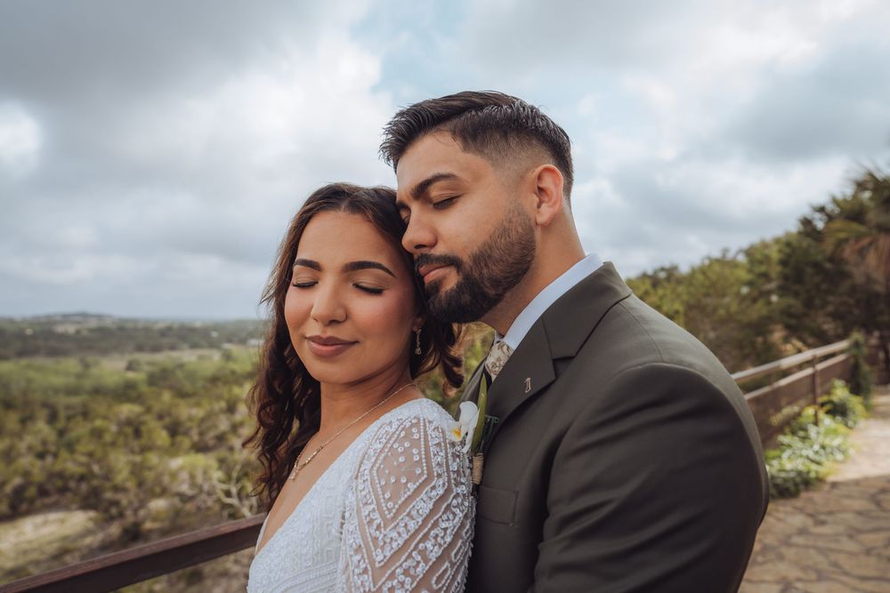 Bride and groom share a tender romantic moment outdoors on their wedding day with scenic greenery backdrop.