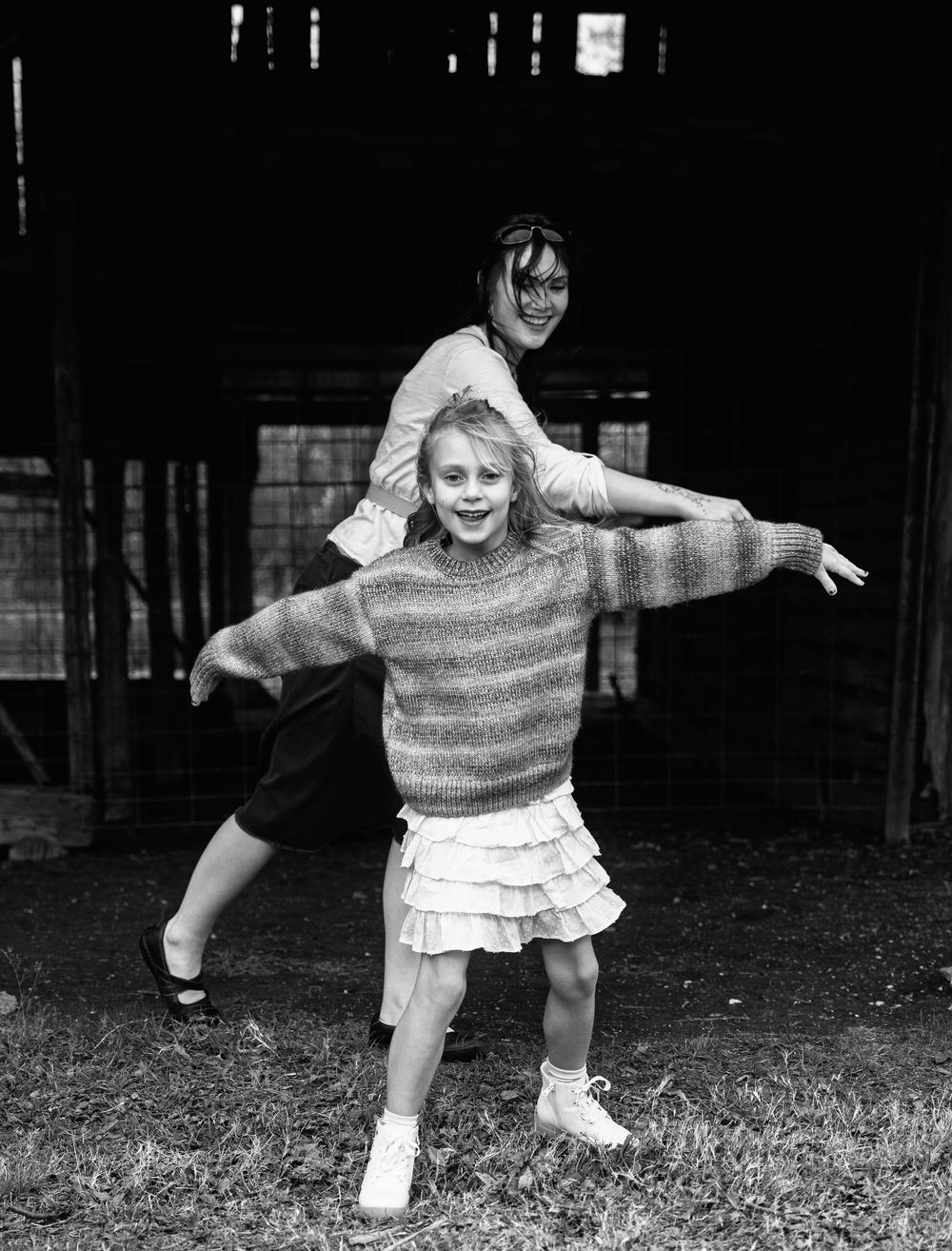 Two girls playing outdoors in black and white photo, older girl riding on younger girl's back, both smiling.