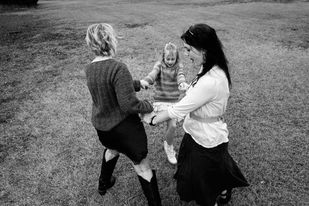 Black and white photo of two women swinging a young child between them outdoors.