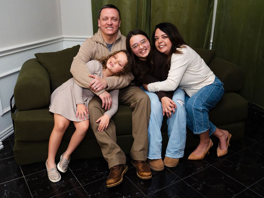 Family of four smiling and posing together on a green couch in a cozy indoor setting.