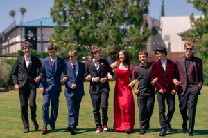Group of seven teens in formal attire walking outdoors on green grass, posing for prom photos. San Diego, CA