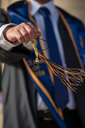 Graduate holding a gold and navy blue graduation tassel with 2026 charm at a graduation photo session. La Jolla, CA
