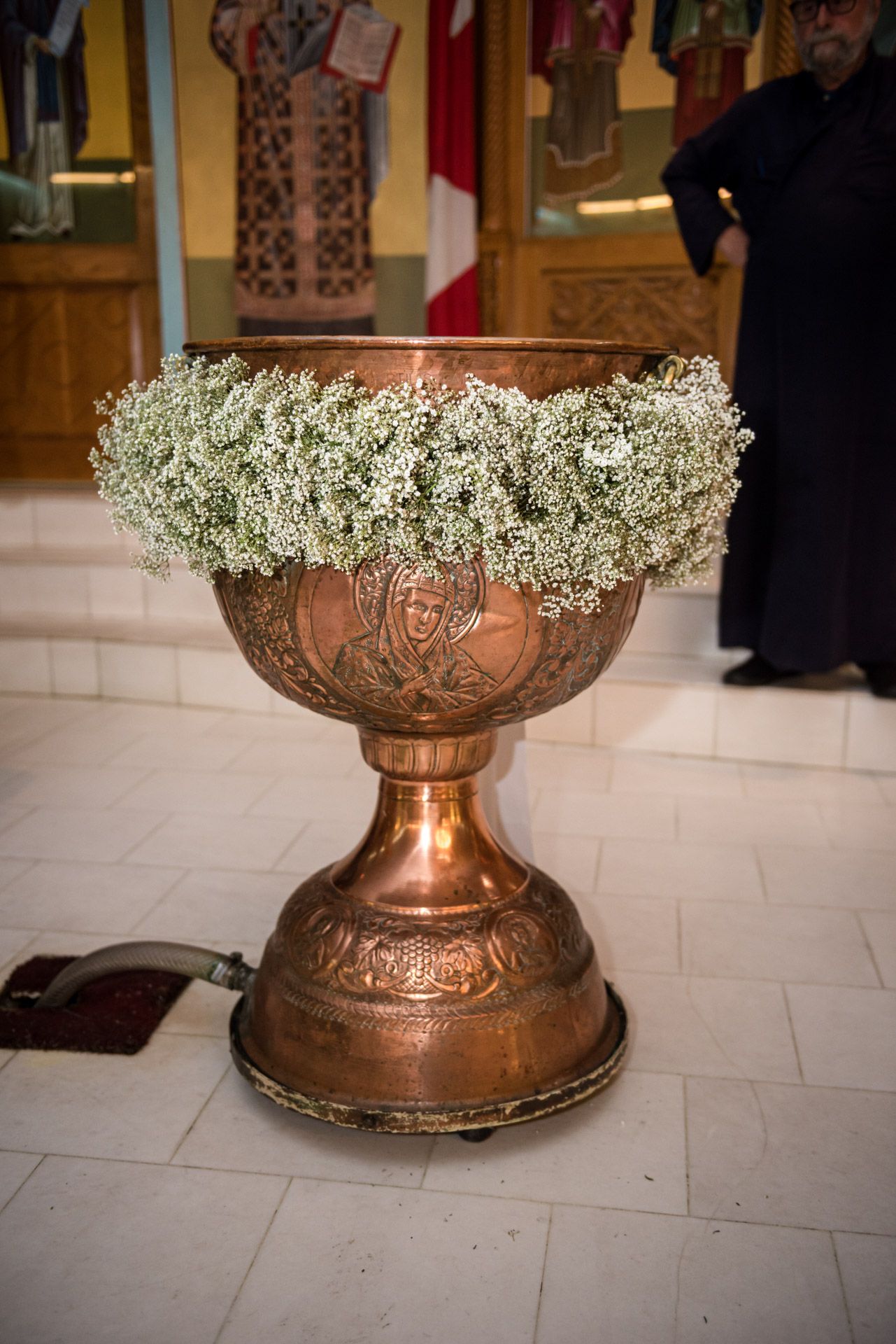 Ornate copper baptismal font decorated with white baby's breath flowers in church.