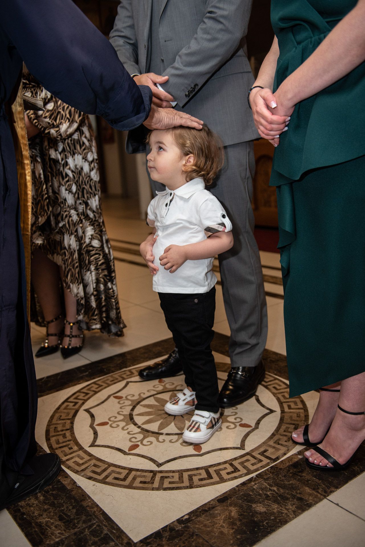 Young toddler in white shirt and black pants receives a blessing during a religious ceremony in church.