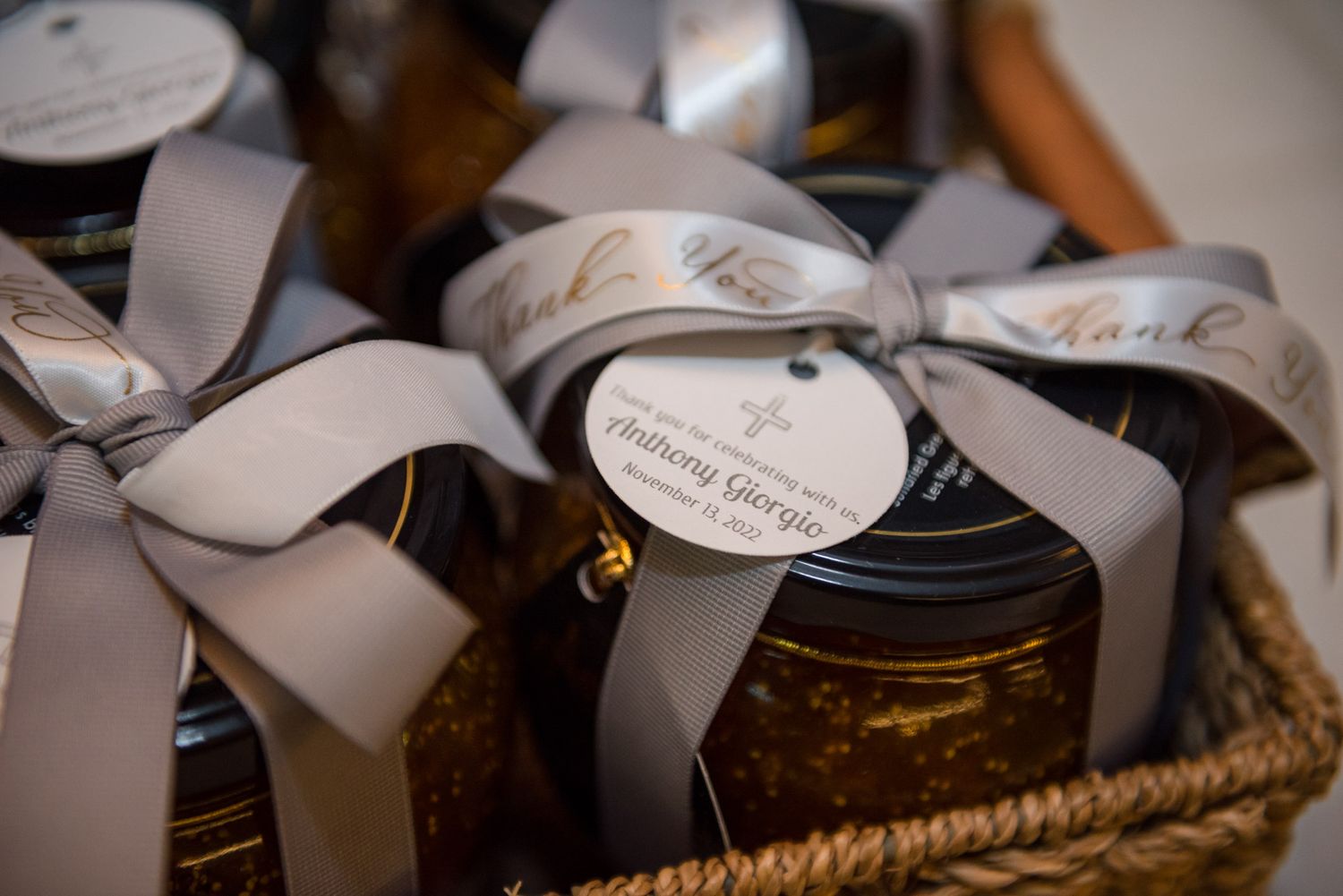 Honey jar favors with gray ribbons and thank you tags in wicker basket.
