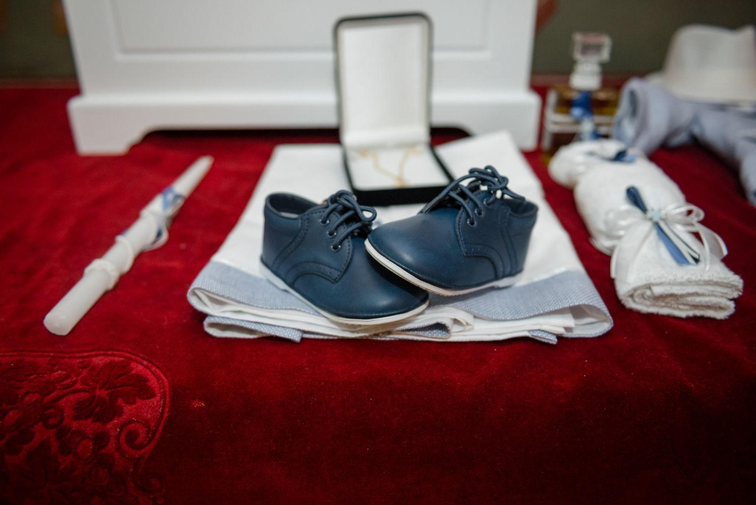 Small navy blue dress shoes on white cloth with candle at baptism ceremony.