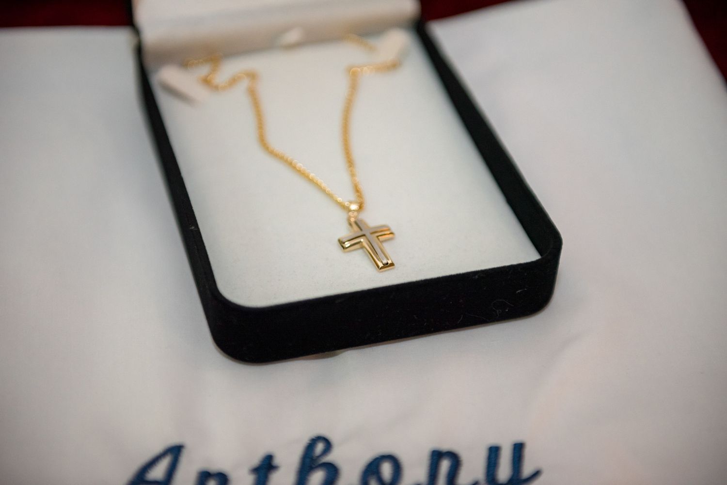 Gold cross pendant necklace in black jewelry box with name Anthony written below.