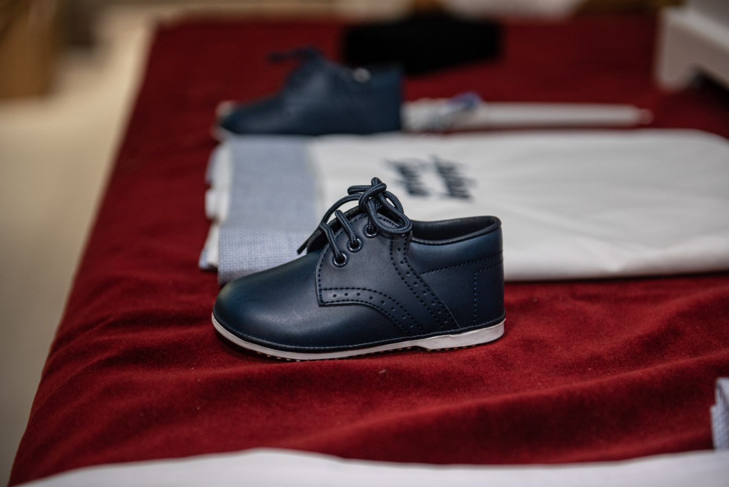 Small navy blue leather lace-up dress shoes for a child displayed on a red velvet surface.