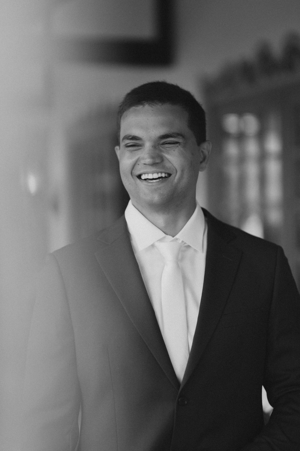 Black and white portrait of a smiling young man in a suit and tie, exuding confidence and professionalism.