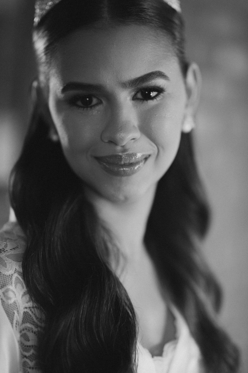 Black and white portrait of a smiling young woman with long hair wearing a lace dress and elegant makeup.