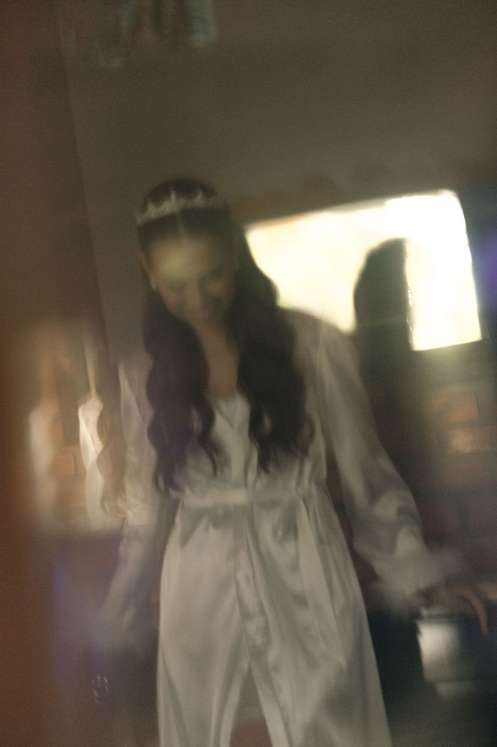 Blurry photo of a woman in a white wedding dress and veil with long dark hair in a dimly lit room.