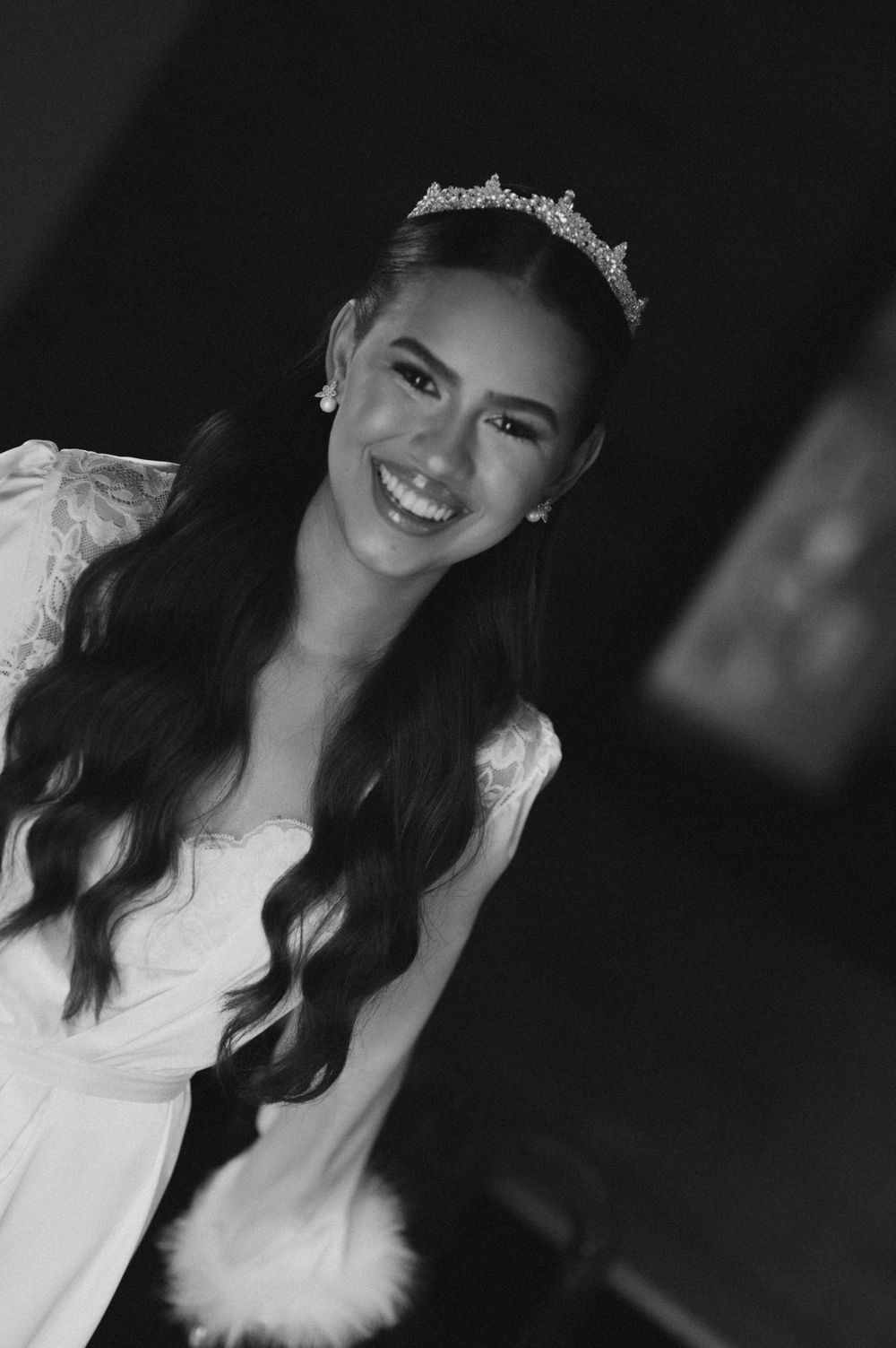 Smiling young woman wearing a tiara and white dress, black and white portrait photo.
