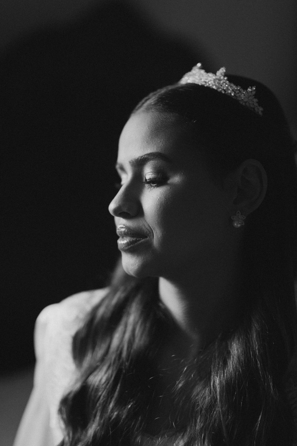 Black and white portrait of a young woman wearing a tiara and earrings, smiling softly in profile view.