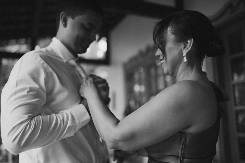 Black and white photo of a woman smiling while adjusting a man's shirt collar at a formal event.