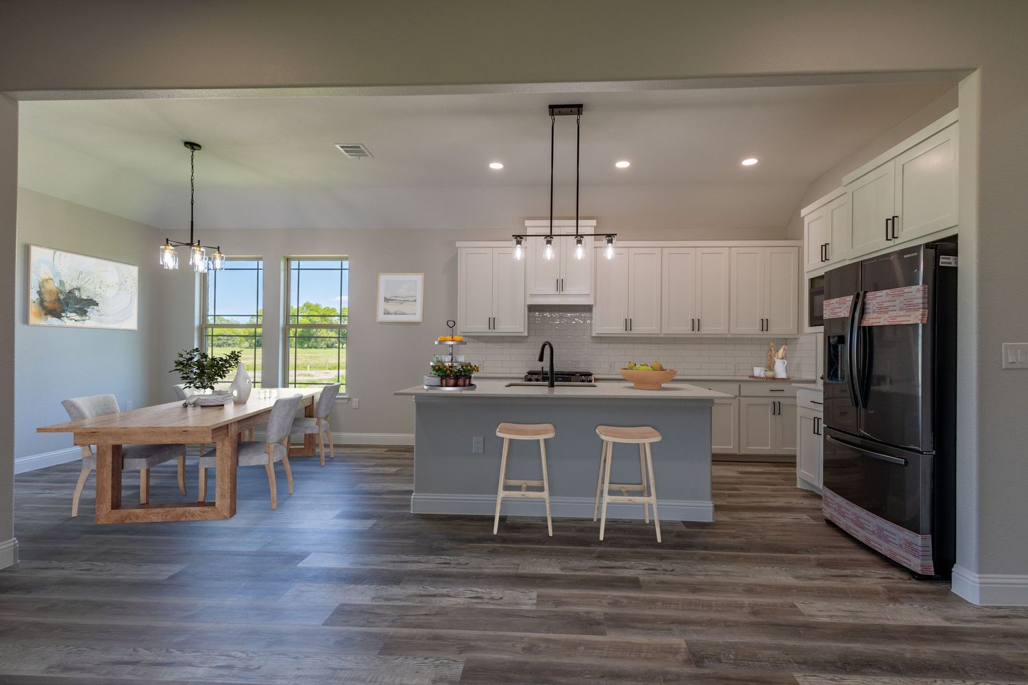 Bright open floor plan kitchen and dining area with modern fixtures and gray wood flooring.