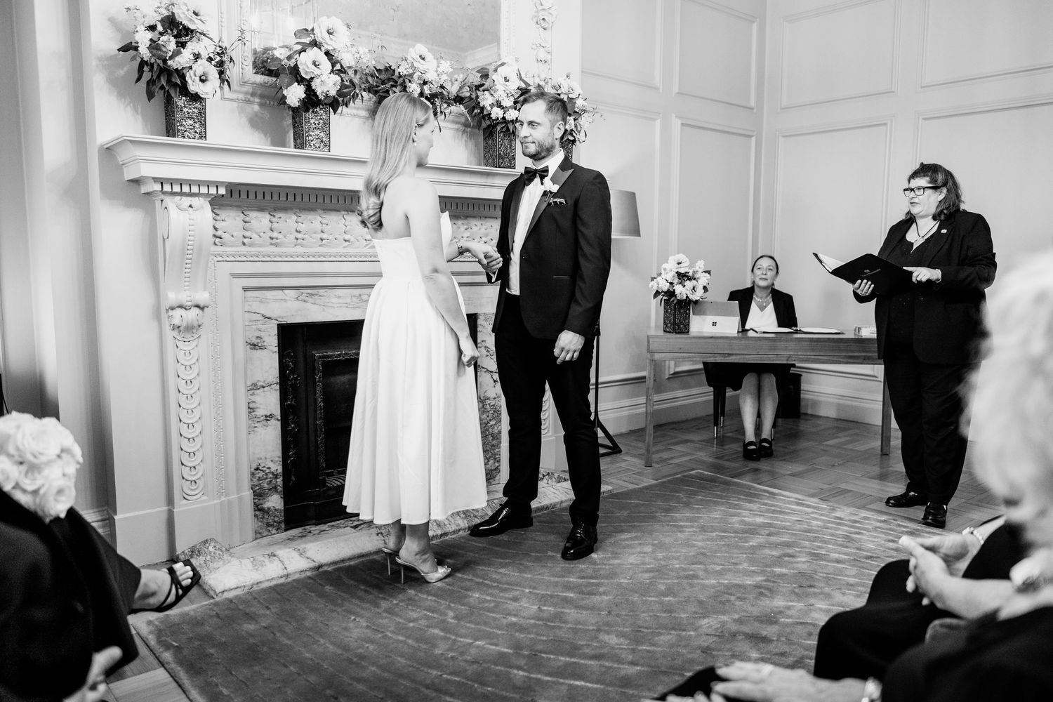 Elderly couple sharing a joyful moment at their wedding ceremony, surrounded by guests in elegant attire.