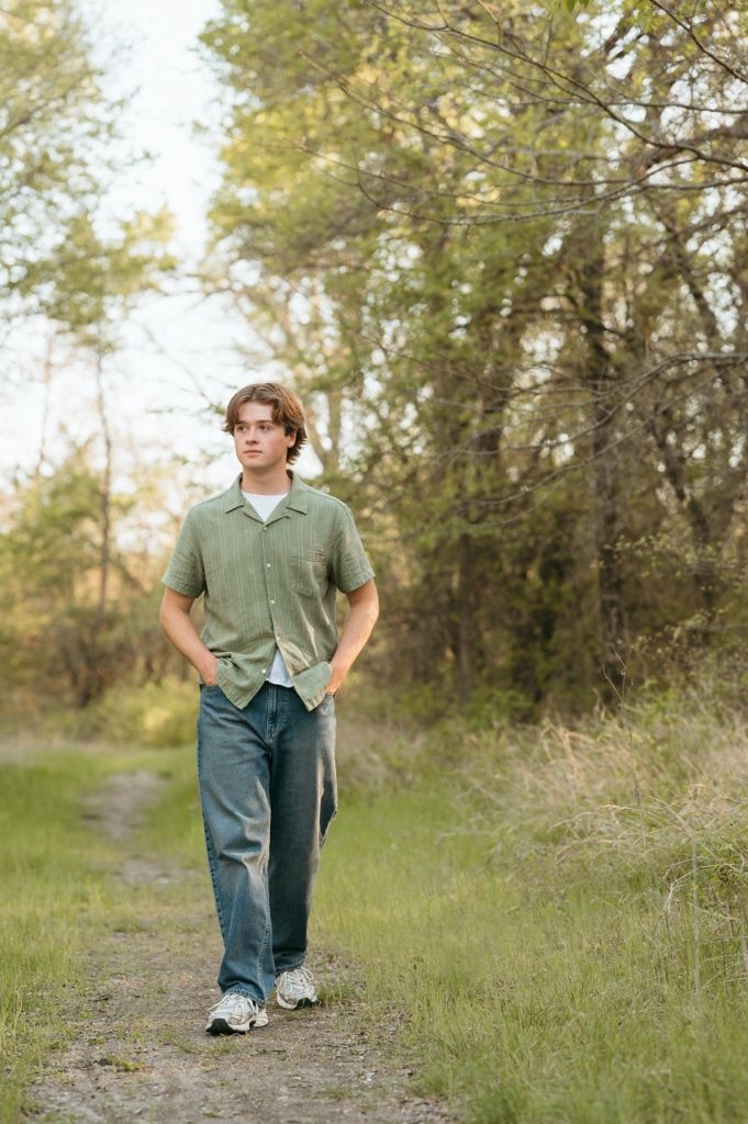 Teen boy in green shirt and jeans walking on a nature trail surrounded by trees.