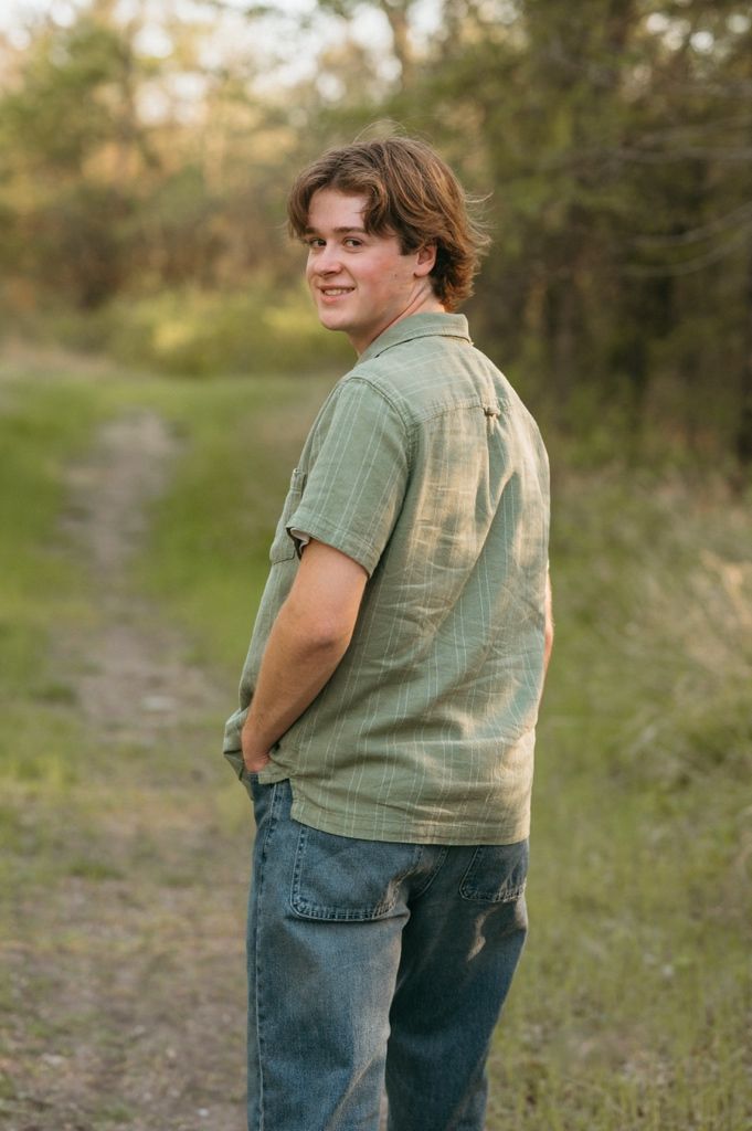 Smiling teen in green shirt and jeans looking back over shoulder on a nature trail.