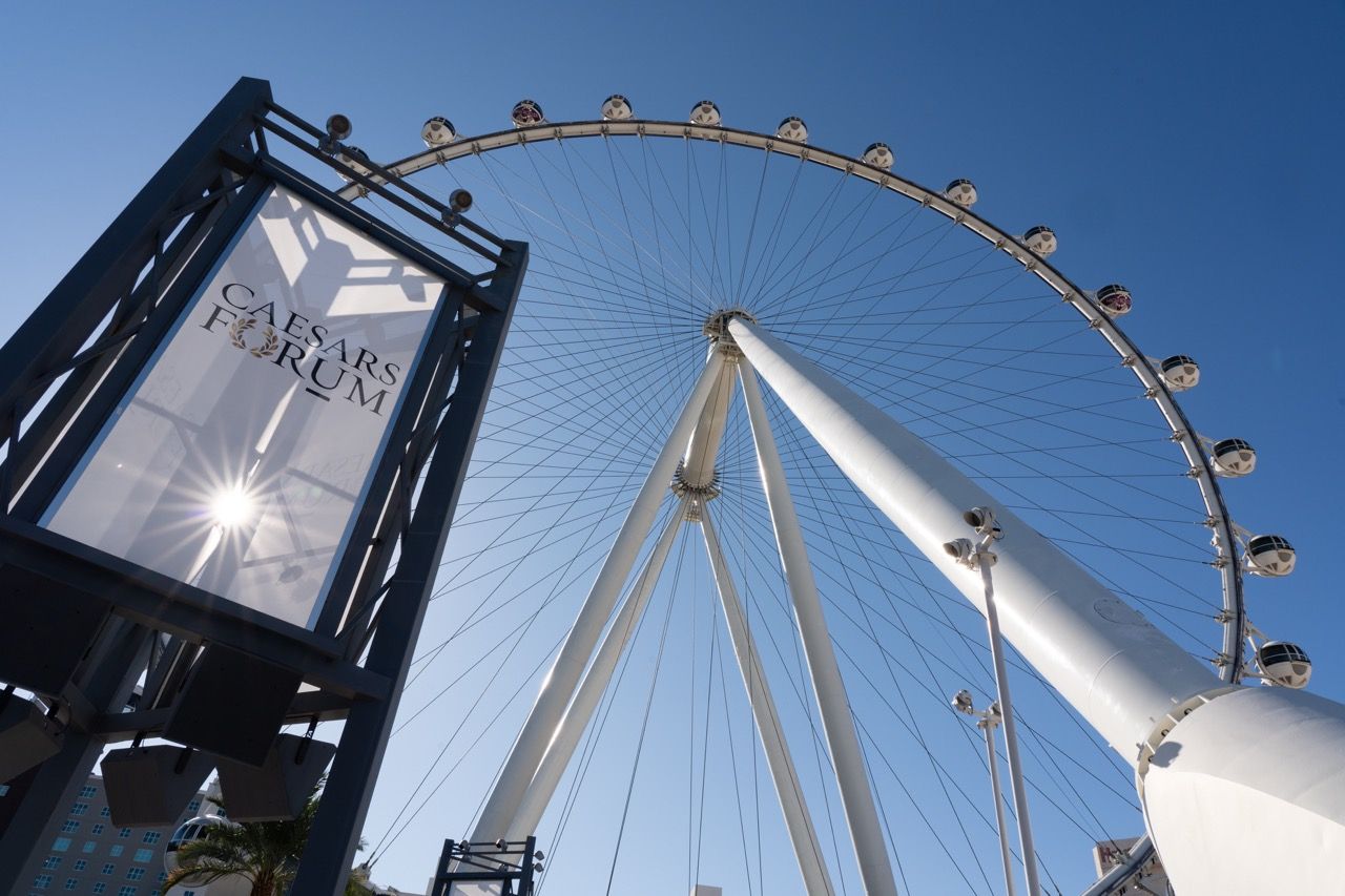 The High Roller observation wheel towers above Caesars Forum sign against a clear blue sky in Las Vegas captured by The Mamones.