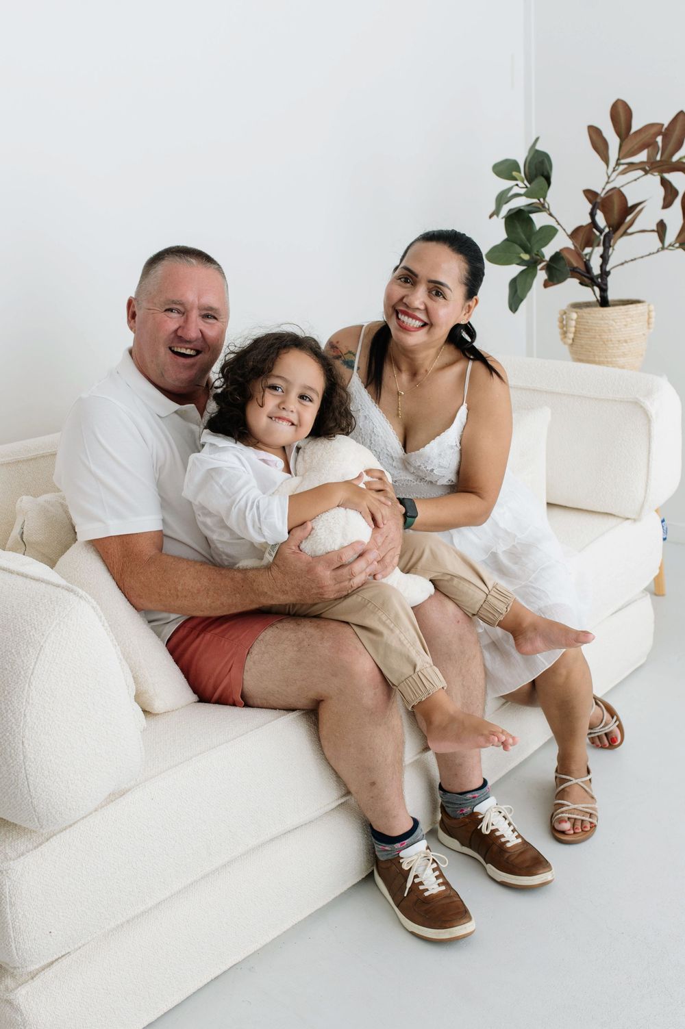 Happy family of three smiling together on a white couch in a bright living room.