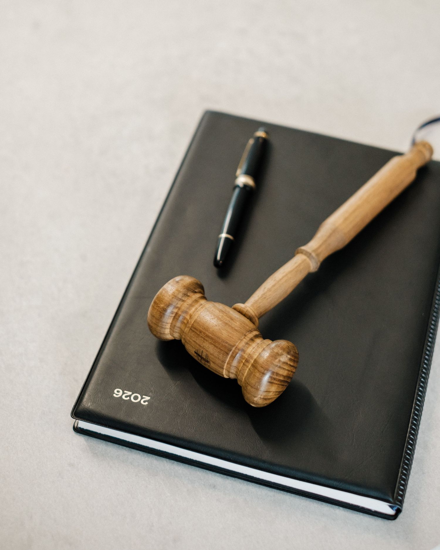 Wooden judge gavel resting on a black 2026 notebook with a fountain pen on a light gray surface.