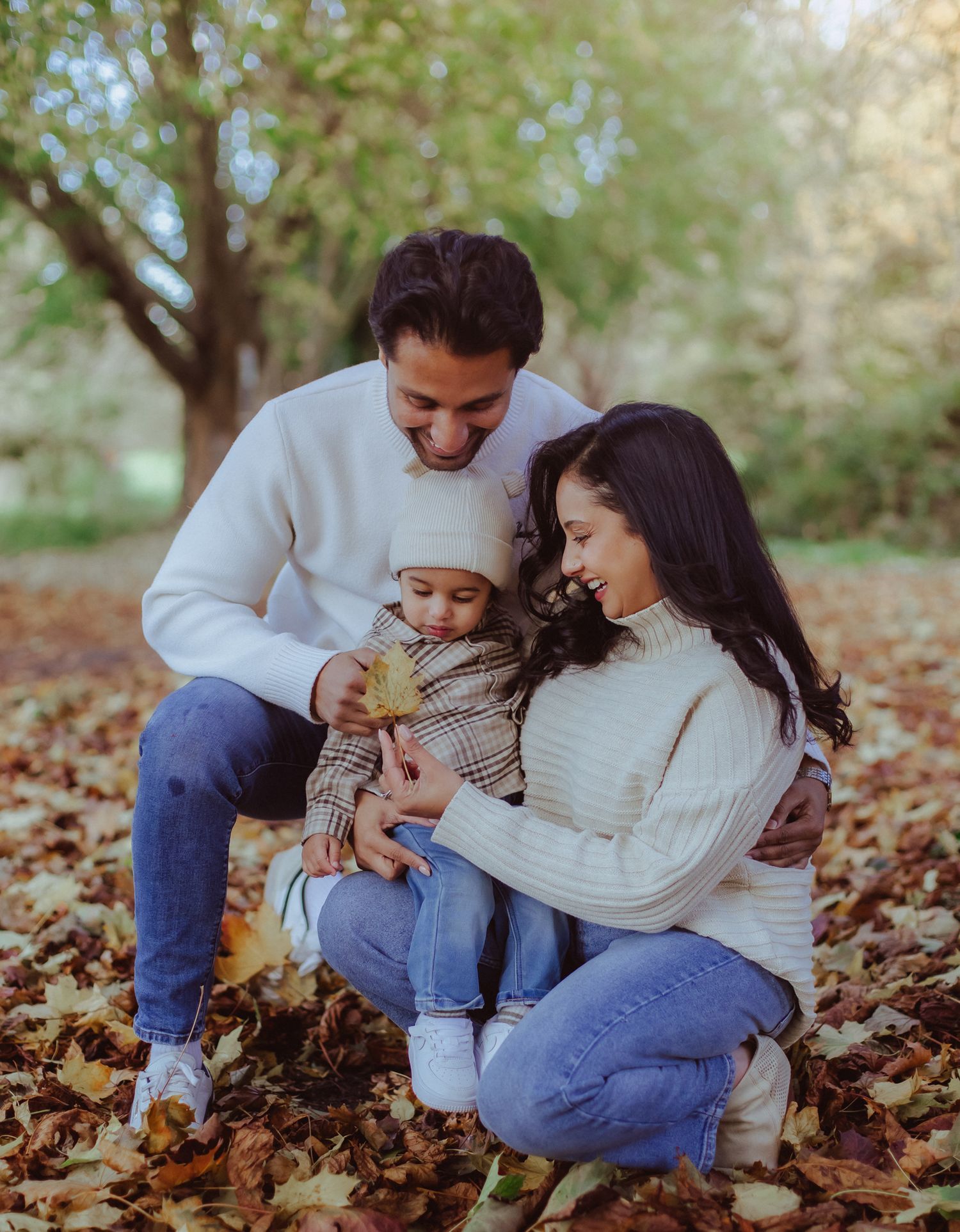 Two babies in white tops and jeans sit together on a white background, looking up curiously. During a family photoshoot in SE London
