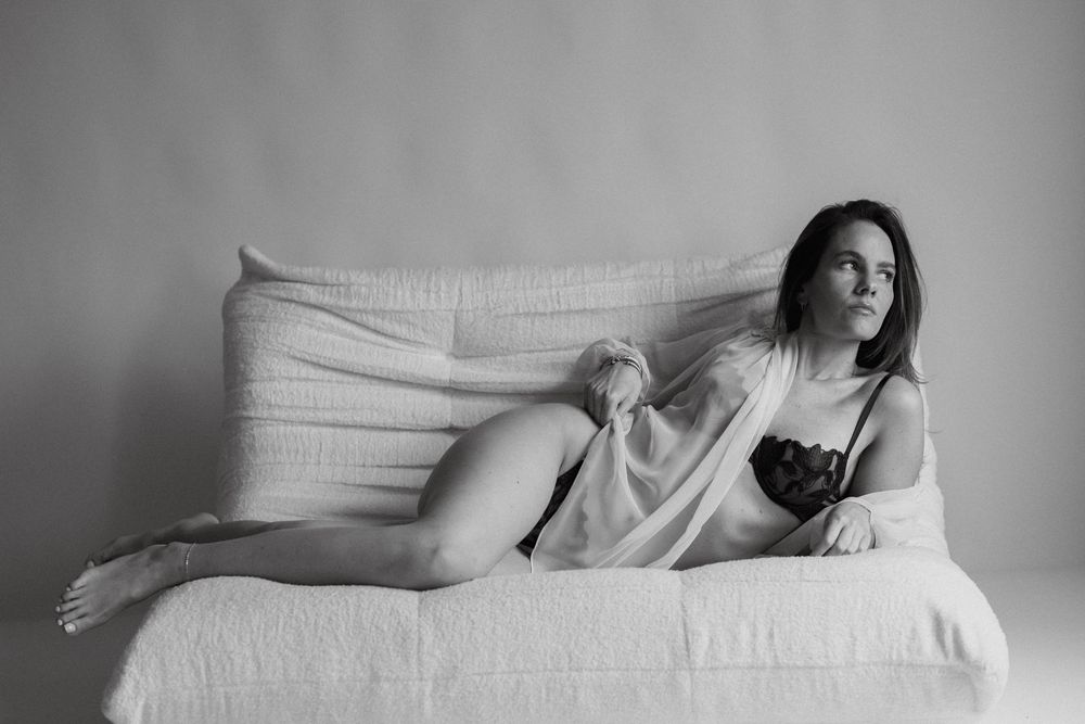 Black and white photo of a woman in lingerie and sheer robe on a sofa.