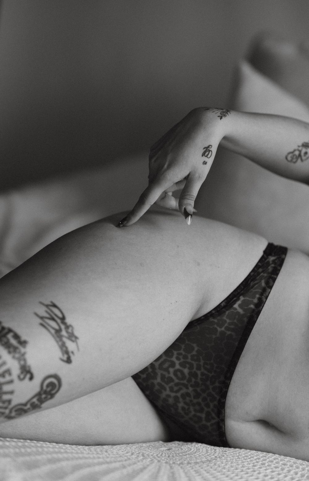 Black and white close-up of a tattooed woman in leopard print lingerie on a bed.