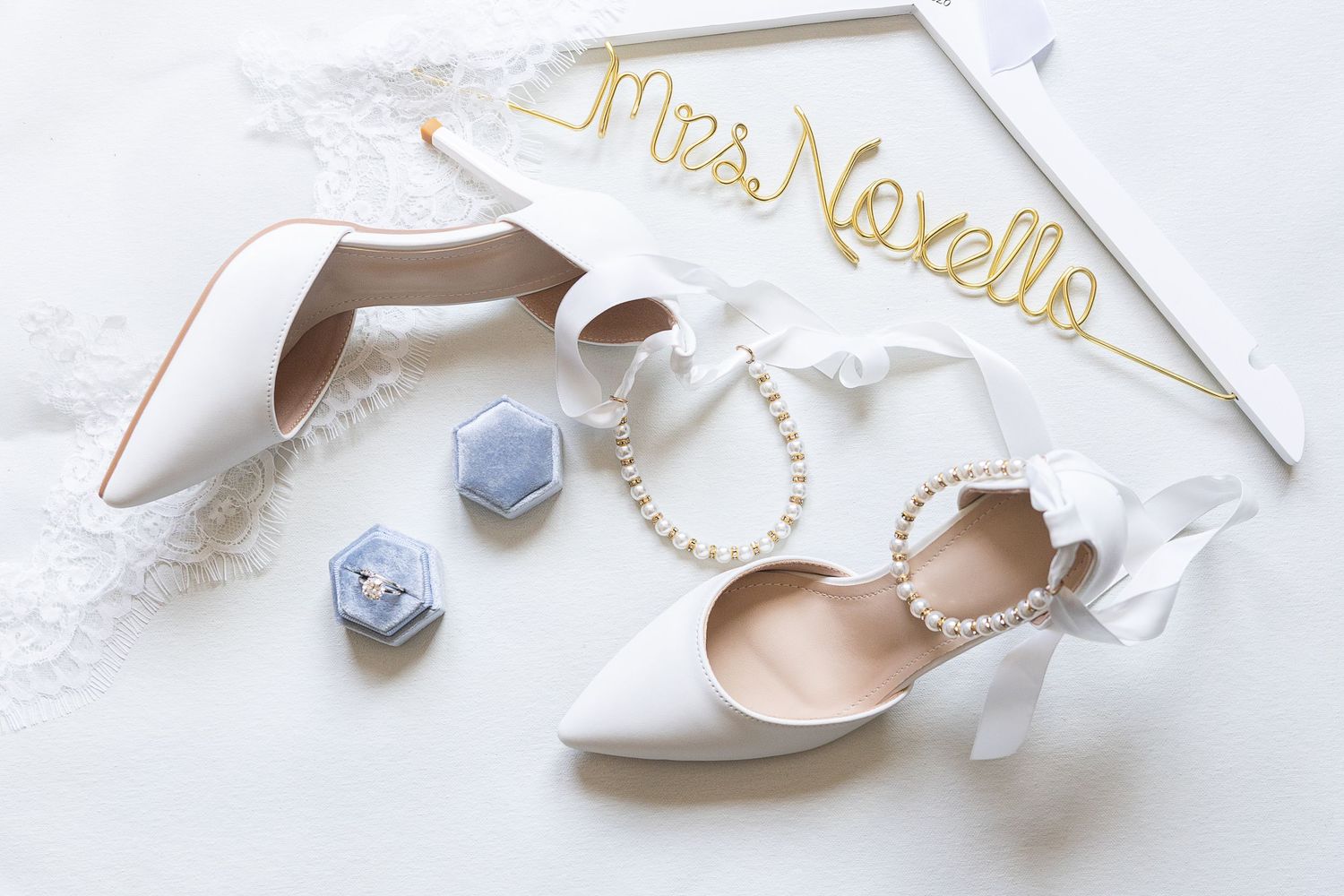 Wedding detail flat lay featuring bridal shoes, engagement ring, pearl accessories, lace robe, and personalized hanger before a Glen Island